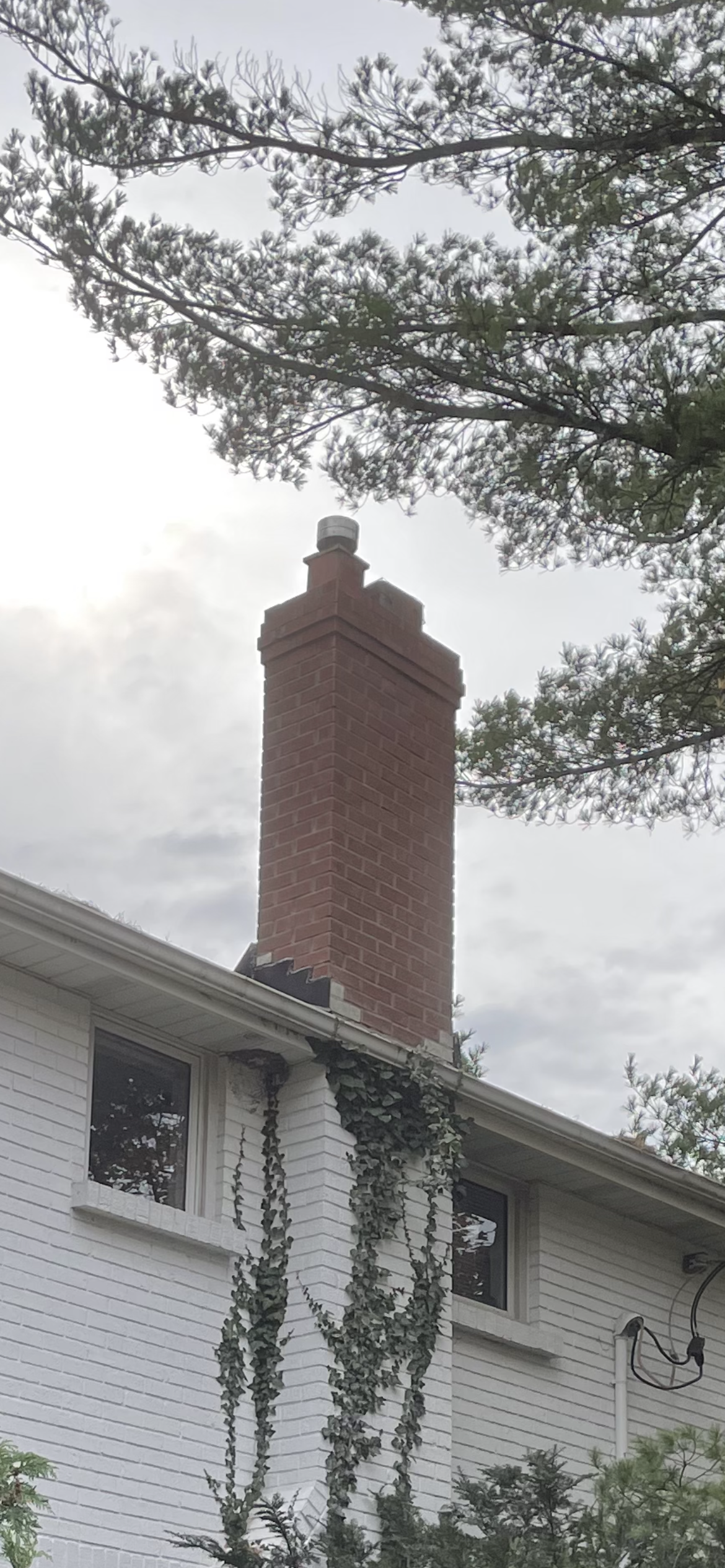 Red brick chimney before restoration, contrasting with white painted brick house in London Ontario